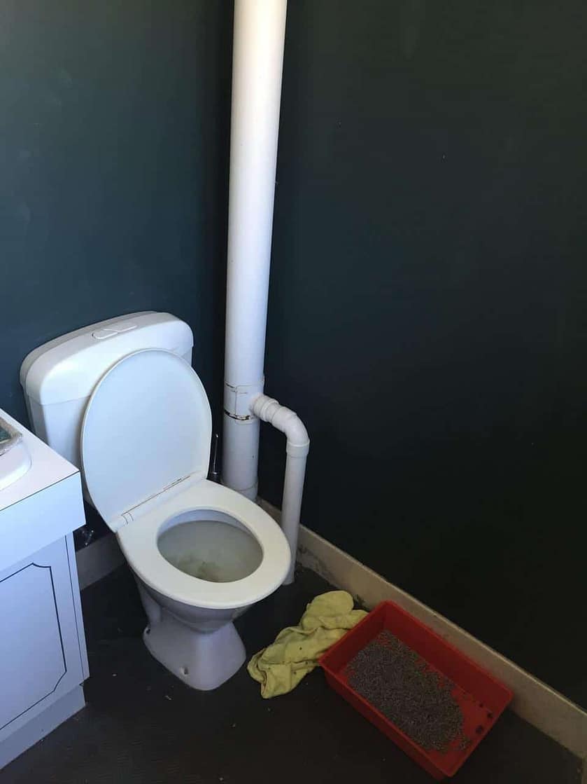 toilet between the bathroom counter and a large pipe